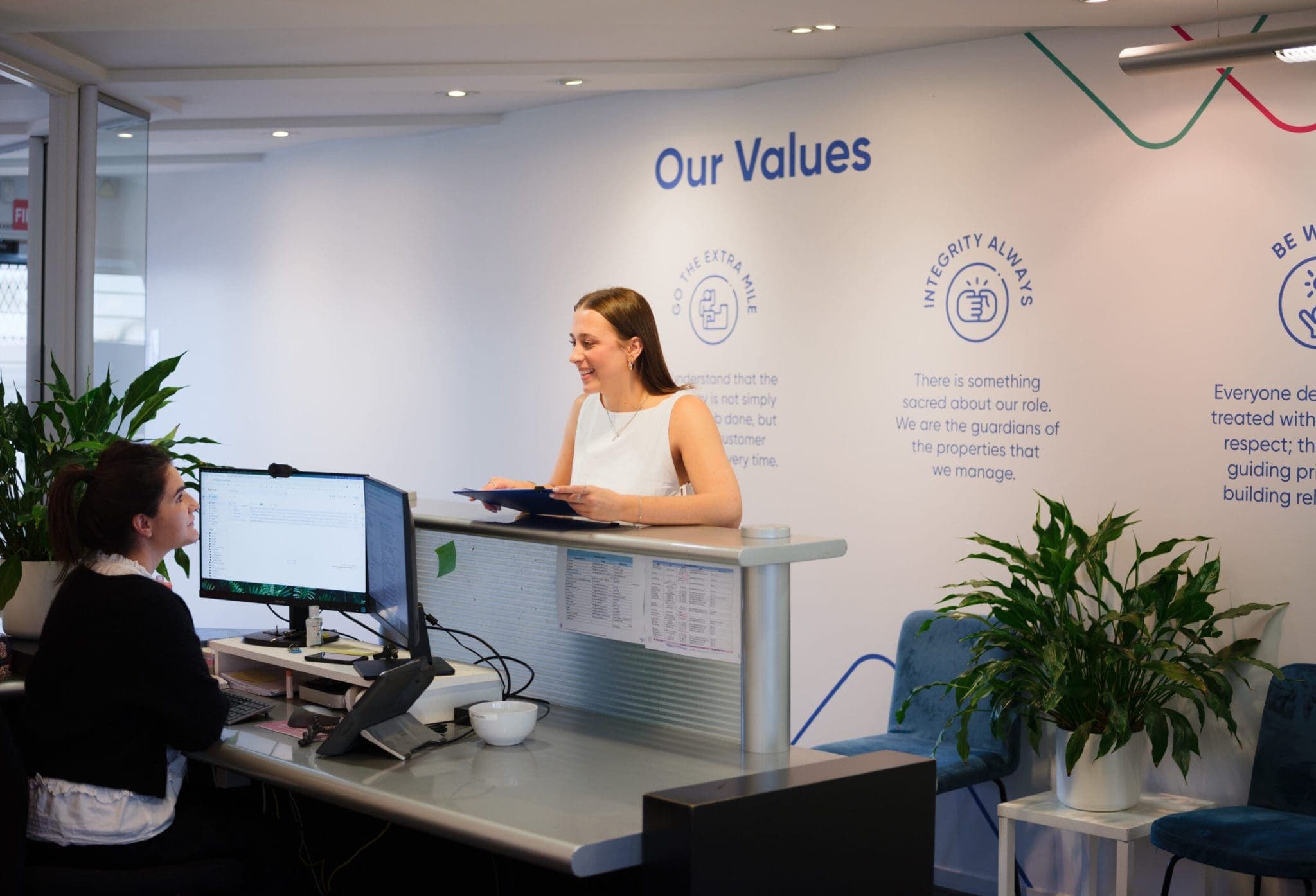 two women in an office setting of Aspire Property reception, one is sitting and other is standing