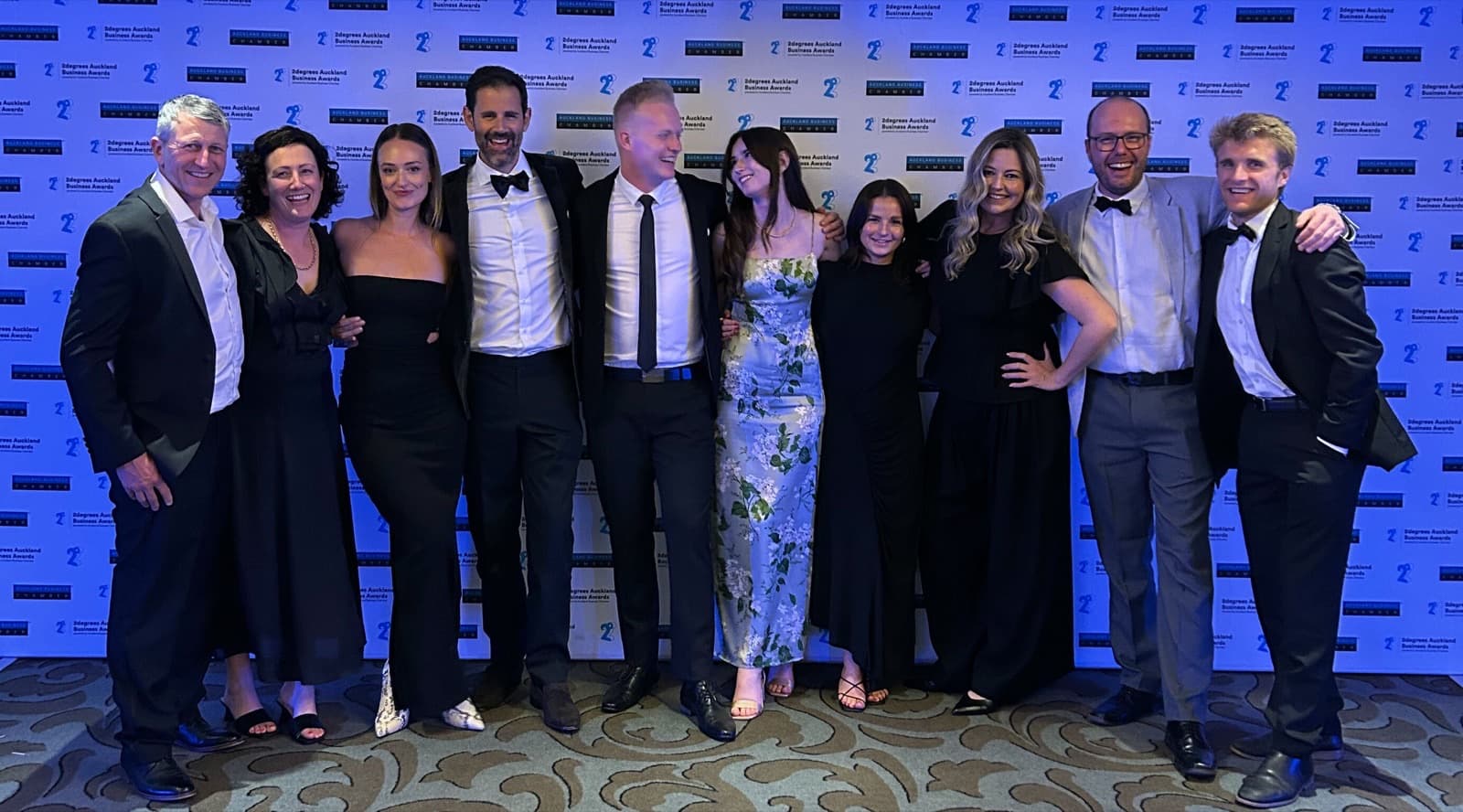 The Aspire Property Management team in black tie at the 2degrees Auckland Business Awards, photographed in front of the awards backdrop