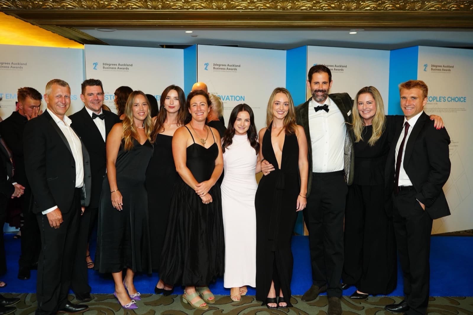 The Aspire Property Management team in black tie at the 2degrees Auckland Business Awards, photographed in front of the awards category boards
