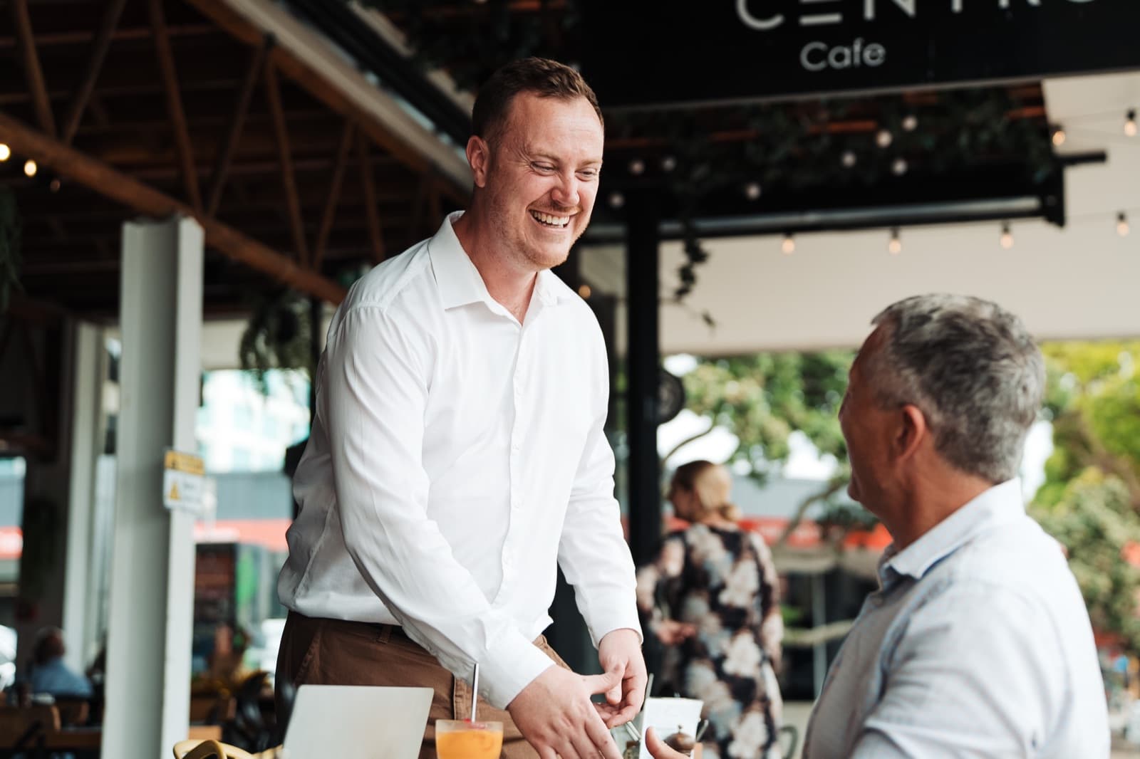 An Aspire property manager smiles as he greets a landlord at an outdoor cafe table