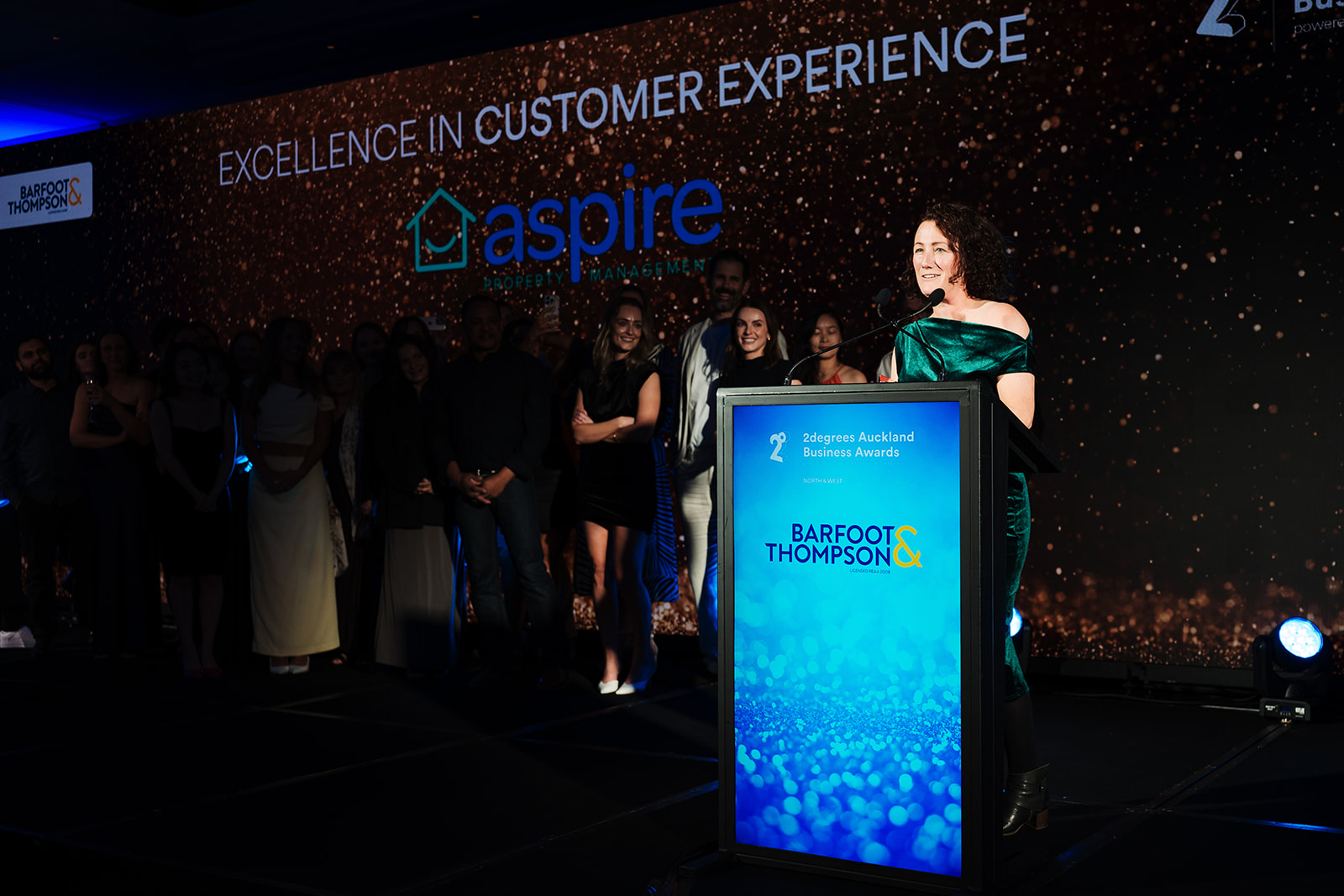 Aspire Property Management general manager Daisy Sievewright accepting the Excellence in Customer Experience award, with the Aspire team on stage behind her